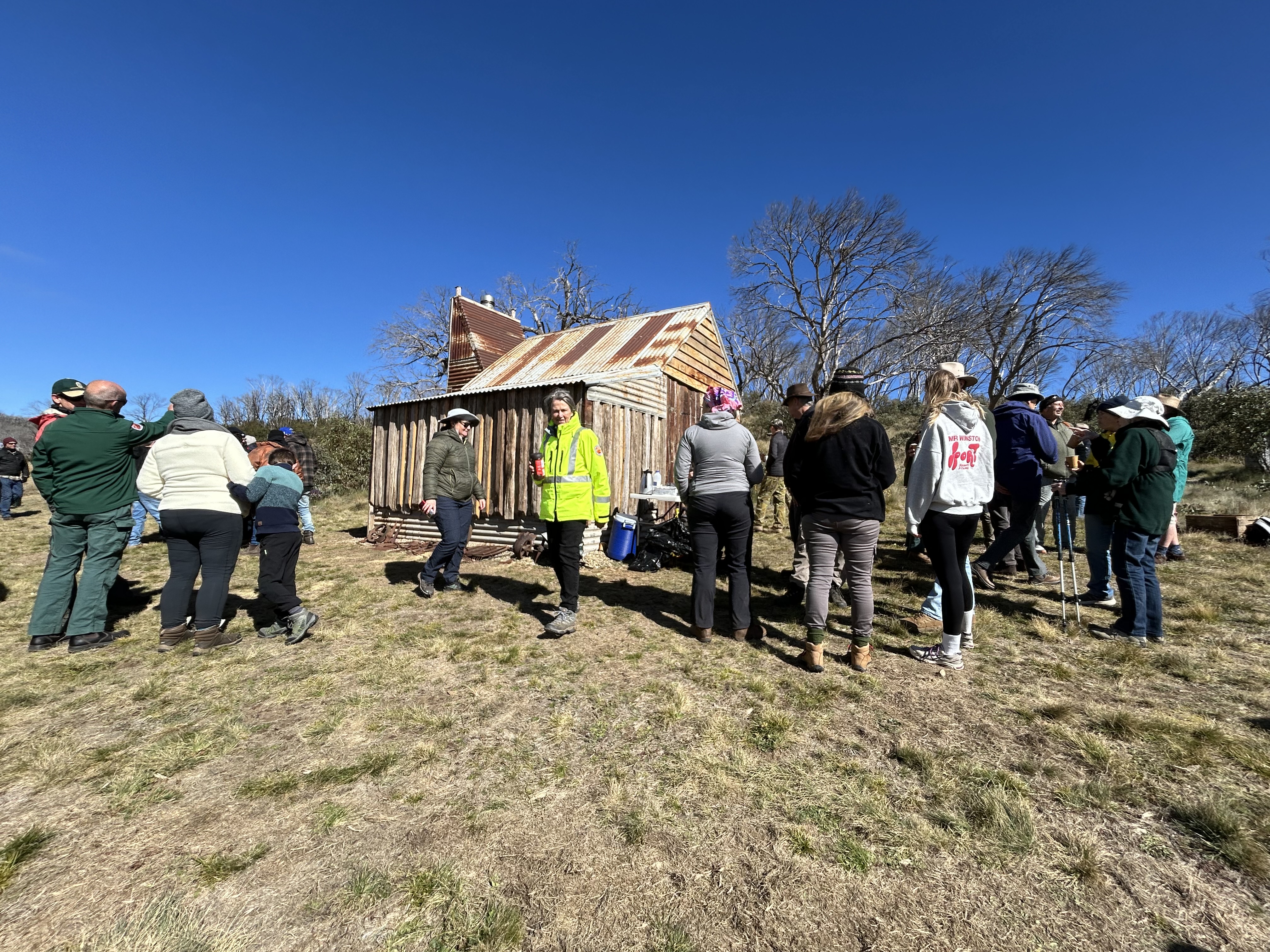 A group of people gathers around the newly rebuilt Four Mile Hut for its reopening